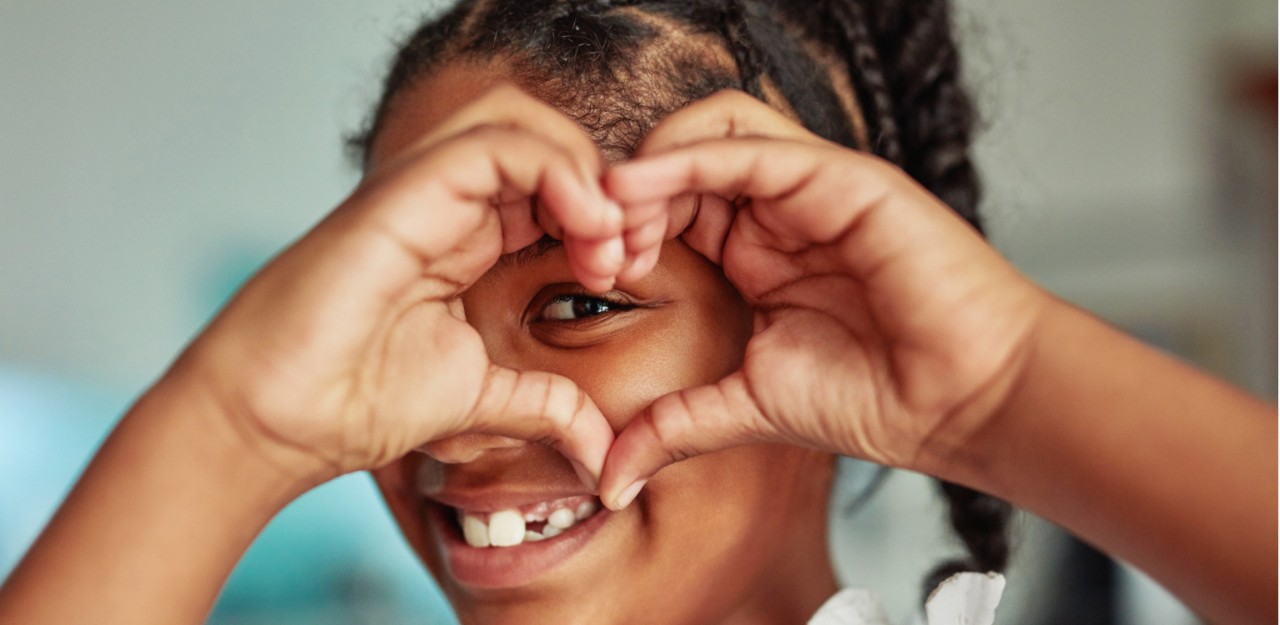 Photo of a child smiling with making a heart with their hands