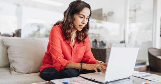 Photo of a woman sitting on a couch while working on her laptop 