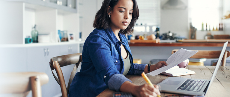 Photo of a woman sitting at a table and working on her laptop 