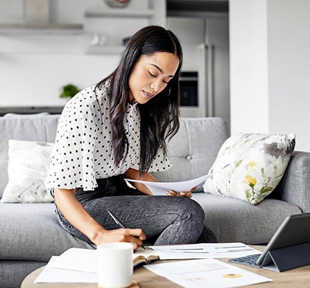 Photo of a woman in her den, working on some documents in front of her laptop 