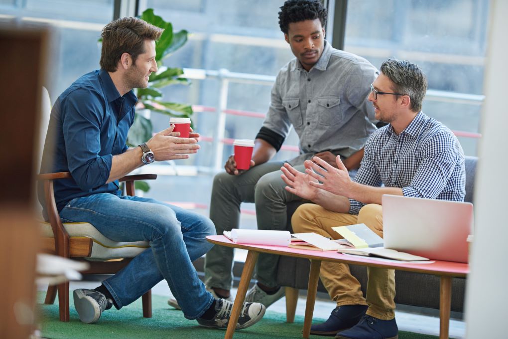 Three people sitting in a public place, chatting with coffee around a table.