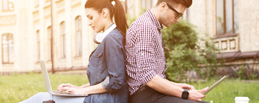 Man and woman sitting back to back looking at their devices