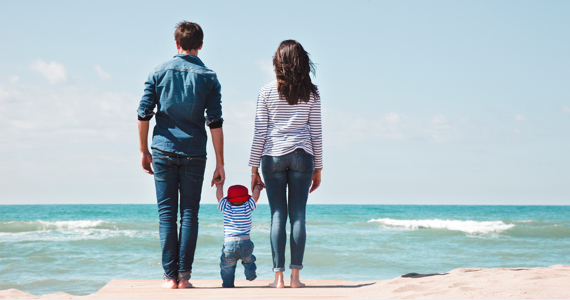 Parents hold toddler by the hand by the sea