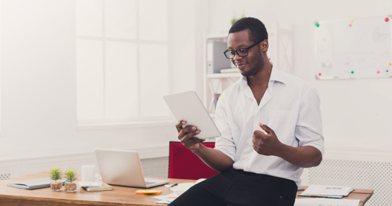 Young man sitting on his desk smiles while looking at a pad