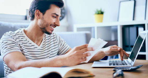 Young man holding notes and using laptop