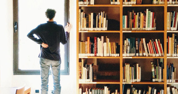 Man looks out window next to bookcase