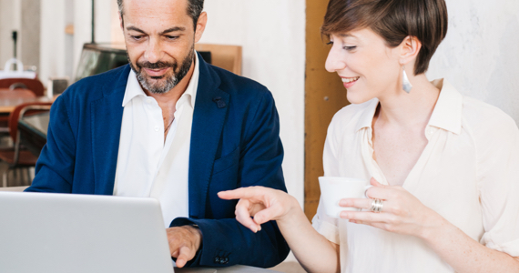 Young woman holding a cup of coffee looks at a computer screen with a man sitting next to her