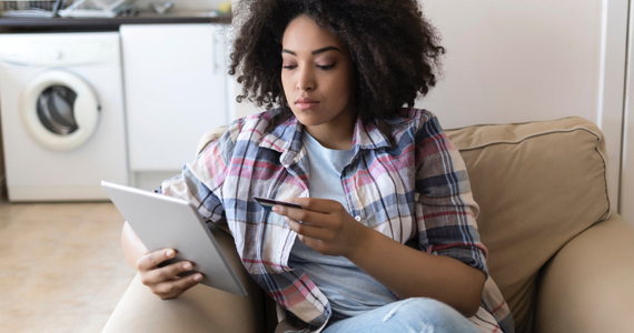 Young woman sitting in an armchair holds a pad in one hand and a bank card in the other