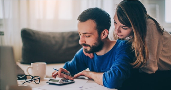 Woman puts her hand on the shoulder of a man sitting at a desk and using a calculator