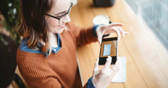 Young woman takes a photo of a cheque with her phone