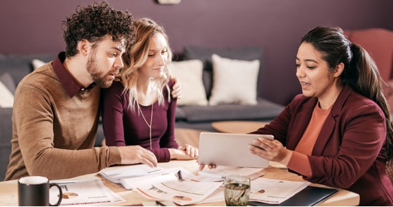 Advisor and young couple sitting at a dining table look at a pad