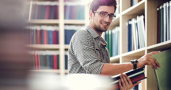 Young man standing in front of a bookshelf smiles