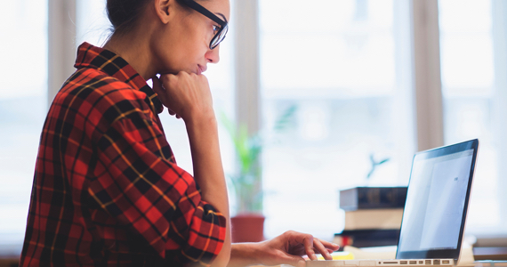 Young female student with glasses and checkered shirt looking at her computer screen