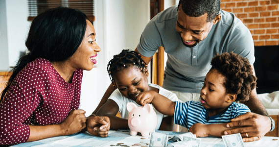 Parents with their two kids smiling and playing with a piggybank. 
