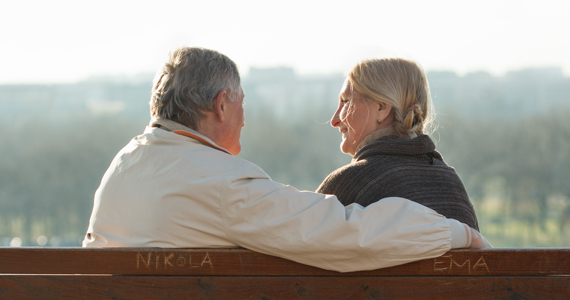 Retired couple on a park bench smile at each other