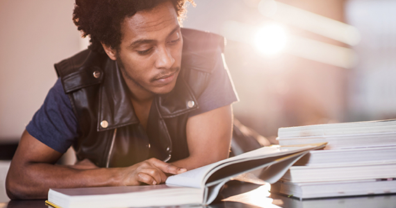 Young student with leather jacket reads in a library