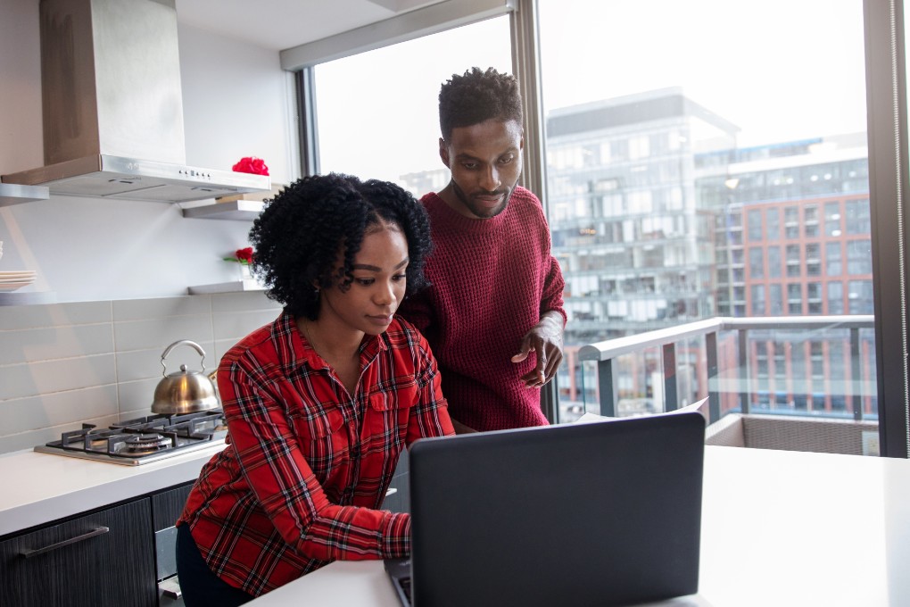 Young couple standing in the kitchen watching a computer