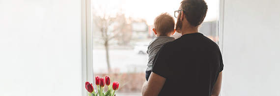 Man holding a baby in his arms in front of a window