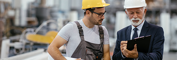 Photo of a construction worker and a businessman wearing hard hats at a construction site