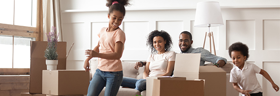 Photo of two adults and two children playing between cardboard boxes in a new home