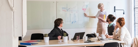 Four people discuss a diagram in a conference room