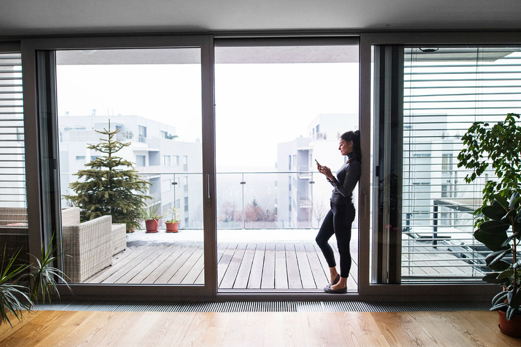 Young woman near a window looking at the declaration of co-ownership of her building on her cellphone. 