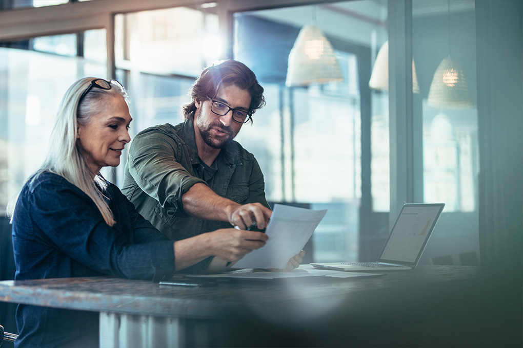 A man and a woman in an office looking at a laptop.