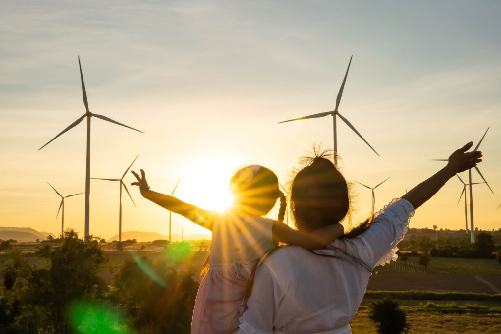 A mother and her daughter look at wind turbine spinning