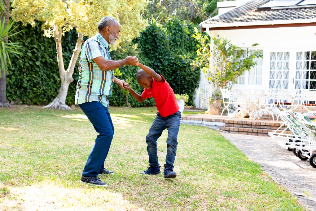 A grandfather and his grandson dance in the family garden.