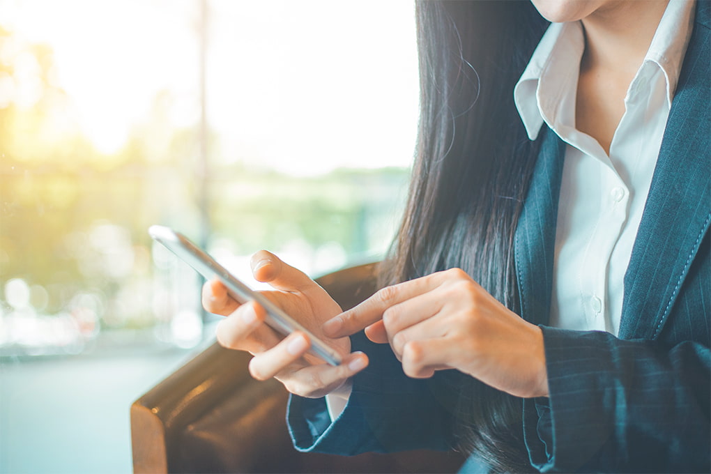 Image of a woman’s hand holding a cell phone and a cup of coffee on the table.