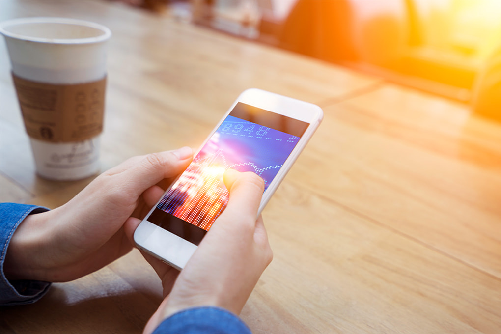 Image of two hands holding a cell phone on a table and a glass of coffee.