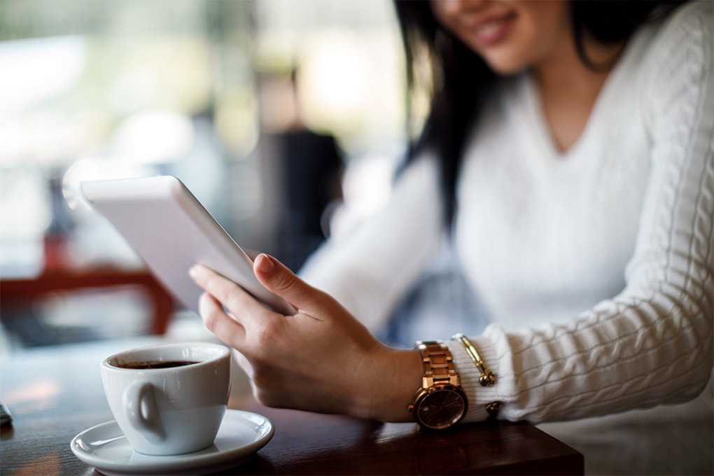 Image d’une main de femme qui tient son téléphone cellulaire et une tasse de café sur la table.