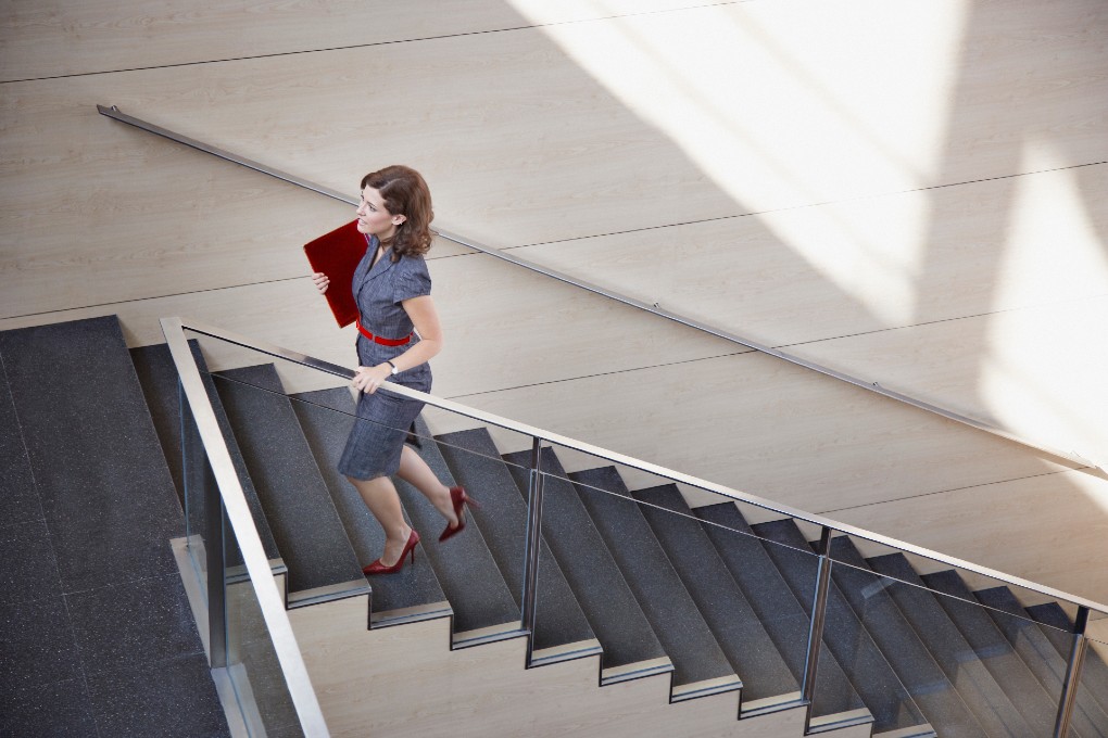 Photo of a woman walking up a large modern staircase with a binder in hand 