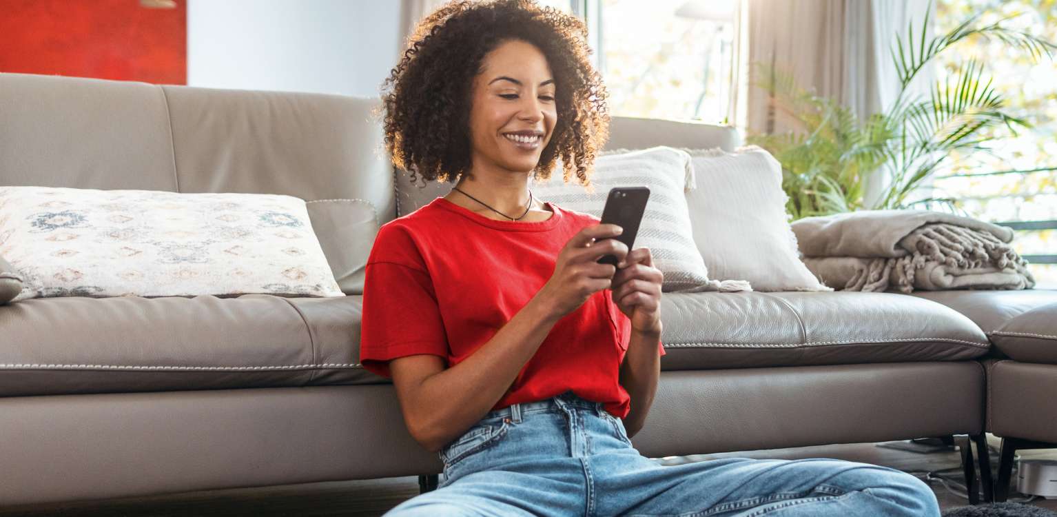 Photo of a person sitting on the floor holding their mobile phone 