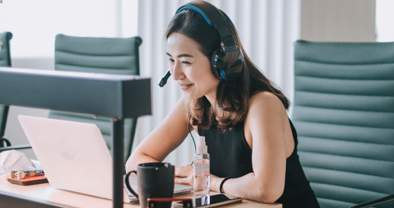 Photo of a woman sitting at desk with a laptop with headphones on attending a virtual meeting