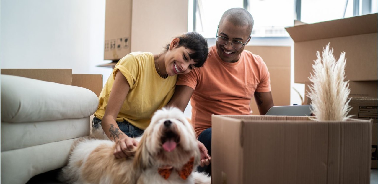 Photo of a young couple sitting with their dog and unpacking moving boxes 
