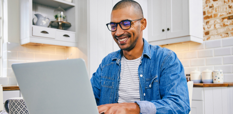 Photo of a person smiling while sitting in their kitchen using their computer