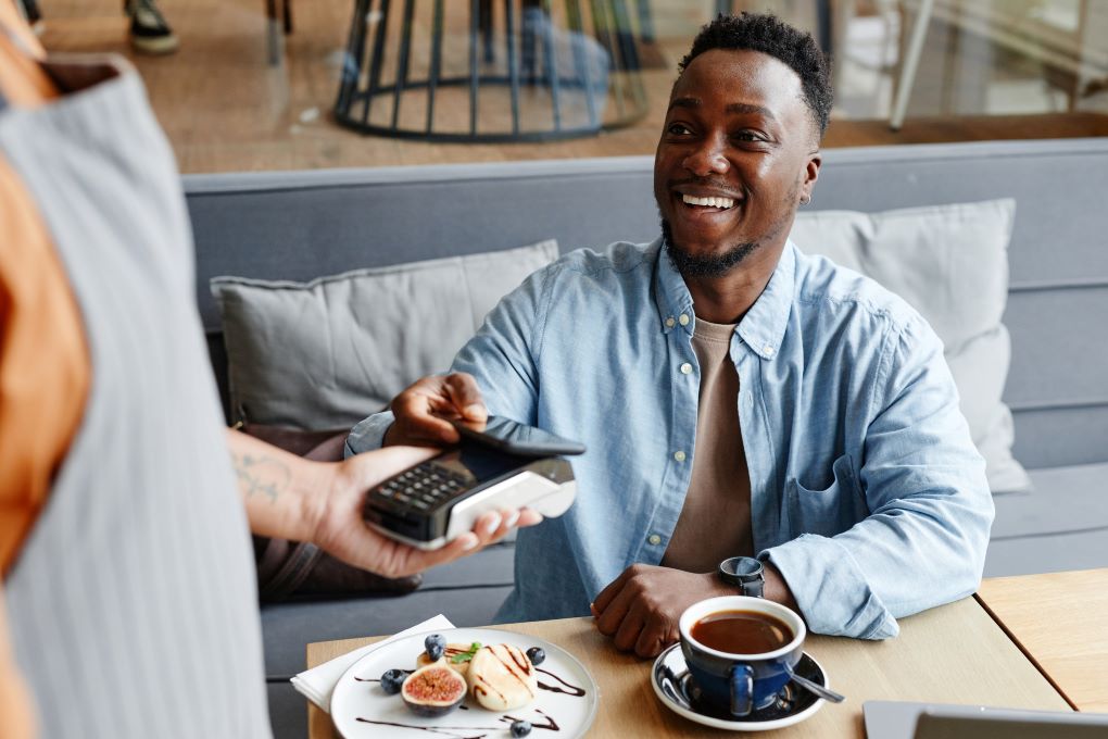 Photo of a person smiling while using their credit card to buy a coffee 