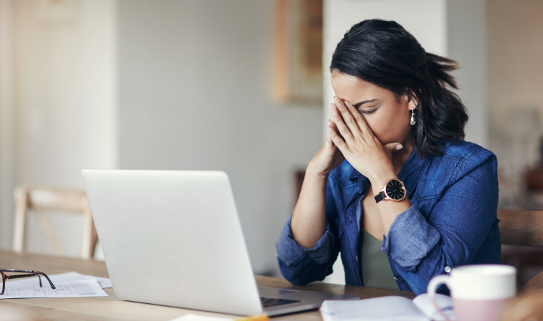 Photo of a person sitting at a table while holding their head in their hands