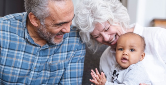 Image of an elderly couple smiling while holding a baby
