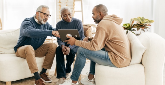 Image of three people looking at a laptop screen while sitting on a couch